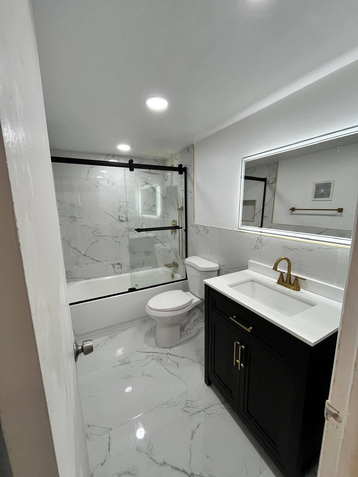 Marble bathroom with black vanity, gold fixtures and LED mirror