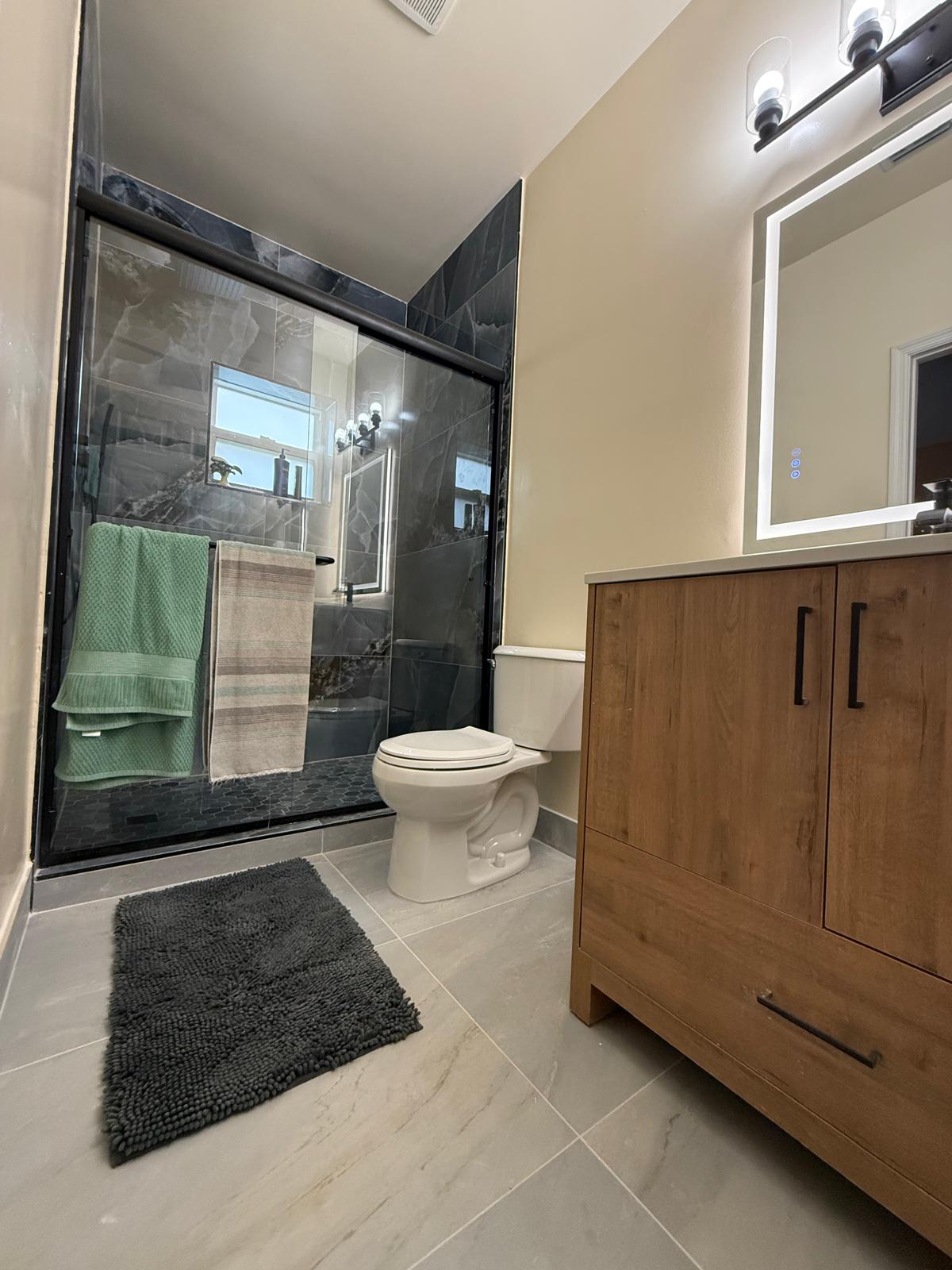 Dark marble walk-in shower with walnut vanity and LED mirror