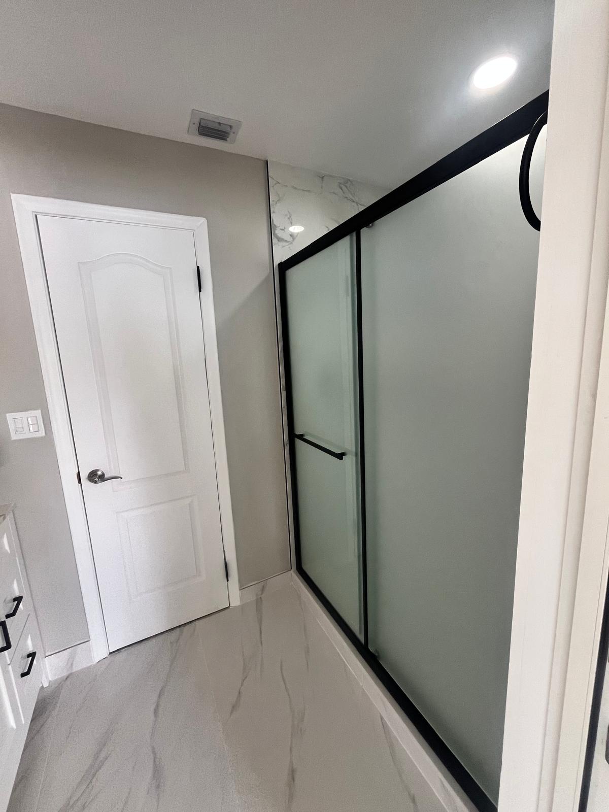 Frosted glass shower enclosure with black hardware on marble tile